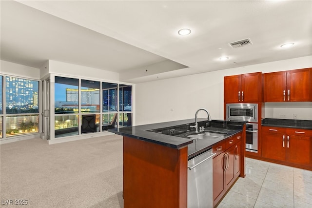 kitchen with visible vents, a center island with sink, dark stone counters, appliances with stainless steel finishes, and a sink