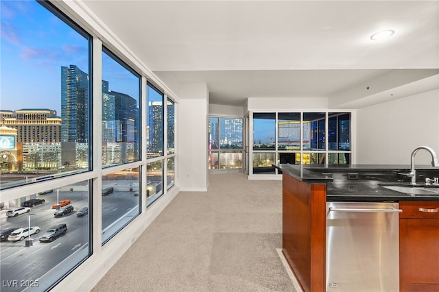 kitchen featuring dark stone counters, light carpet, brown cabinets, a view of city, and a sink