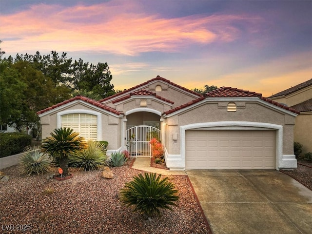 mediterranean / spanish-style house featuring a tile roof, stucco siding, driveway, an attached garage, and a gate