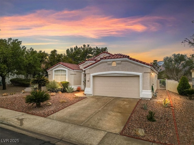 mediterranean / spanish-style home with fence, a tiled roof, stucco siding, a garage, and driveway