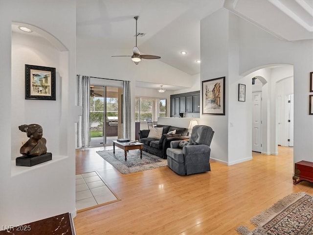 living area with high vaulted ceiling, arched walkways, light wood-style floors, and a ceiling fan