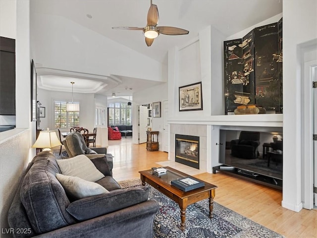 living room featuring a ceiling fan, vaulted ceiling, wood finished floors, and a tile fireplace