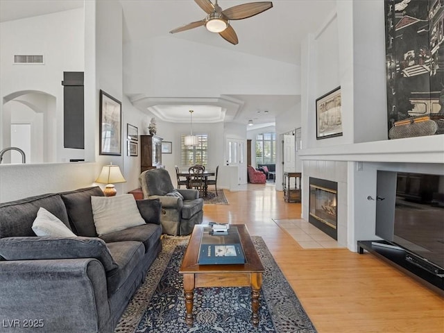 living room with visible vents, arched walkways, light wood-style floors, ceiling fan, and a tile fireplace