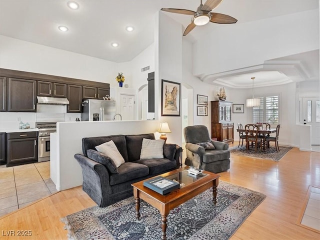 living room with visible vents, ceiling fan, light wood-type flooring, recessed lighting, and a high ceiling