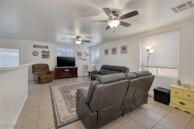 living room with visible vents, baseboards, light tile patterned floors, a textured ceiling, and a ceiling fan