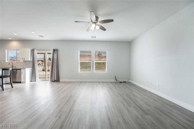 unfurnished living room with light wood-style flooring, a ceiling fan, and baseboards