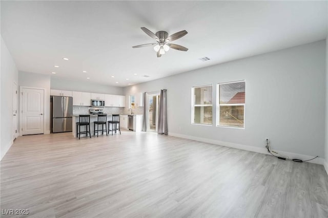 unfurnished living room featuring light wood finished floors, visible vents, baseboards, and ceiling fan