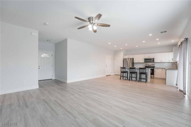 unfurnished living room with baseboards, visible vents, light wood finished floors, and a sink