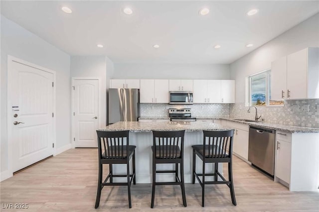 kitchen featuring a center island, appliances with stainless steel finishes, a kitchen breakfast bar, white cabinetry, and a sink