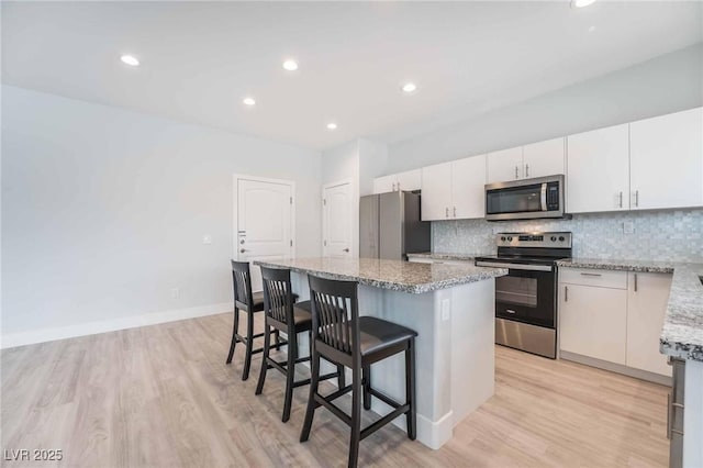 kitchen with light stone counters, appliances with stainless steel finishes, a kitchen bar, tasteful backsplash, and a center island