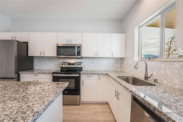 kitchen featuring a sink, tasteful backsplash, stainless steel appliances, white cabinets, and light stone countertops