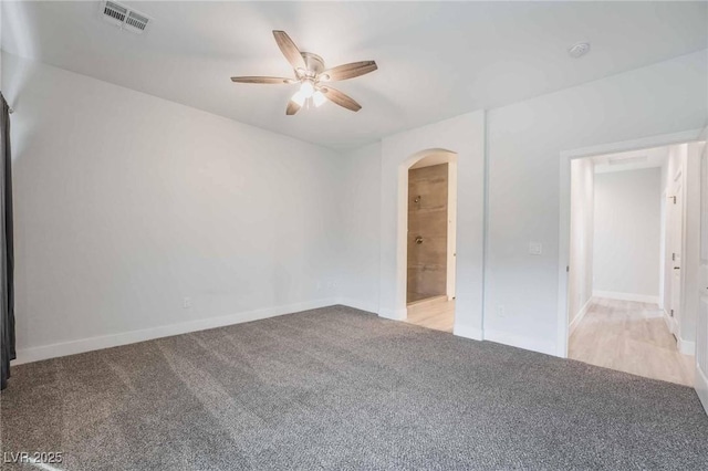 empty room with visible vents, a ceiling fan, arched walkways, carpet flooring, and baseboards