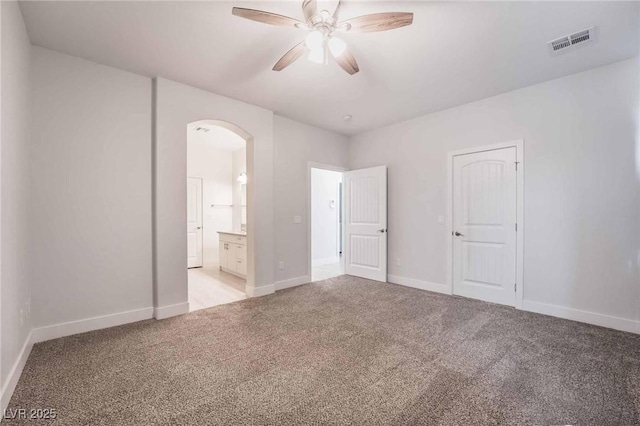 unfurnished bedroom featuring baseboards, visible vents, arched walkways, light colored carpet, and connected bathroom