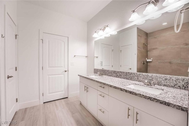 bathroom featuring double vanity, a shower, wood finished floors, and a sink