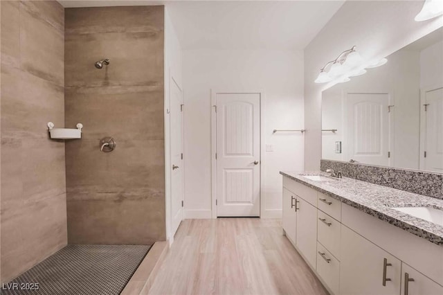 bathroom featuring a sink, tiled shower, wood finished floors, and double vanity