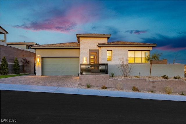 prairie-style home with decorative driveway, stone siding, an attached garage, and stucco siding