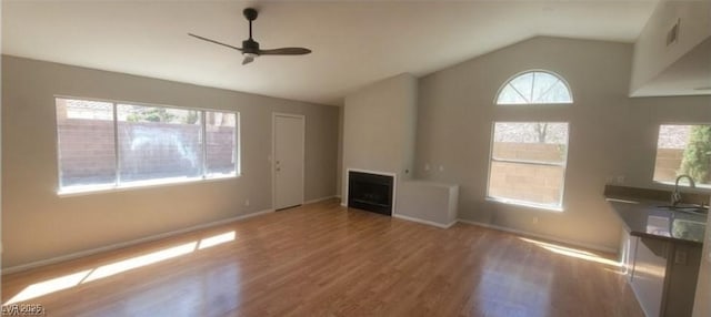 unfurnished living room with a sink, wood finished floors, a fireplace, lofted ceiling, and ceiling fan