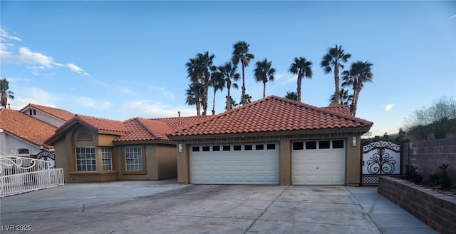 mediterranean / spanish-style home featuring stucco siding, driveway, a tile roof, fence, and a garage