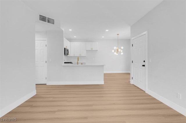 unfurnished living room featuring a notable chandelier, baseboards, visible vents, and light wood-type flooring