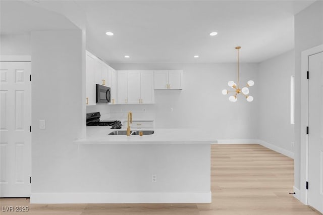 kitchen featuring light wood finished floors, black appliances, a peninsula, white cabinetry, and a sink