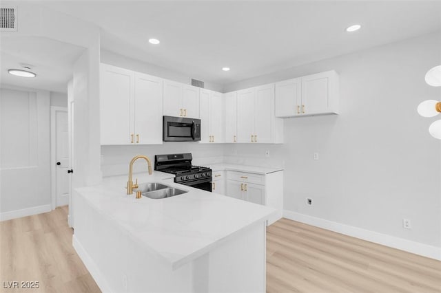 kitchen with light countertops, gas range oven, a peninsula, white cabinetry, and a sink