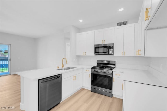 kitchen featuring light countertops, appliances with stainless steel finishes, a peninsula, white cabinetry, and a sink