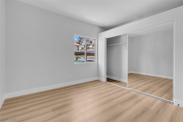 unfurnished bedroom featuring wood finished floors, baseboards, and a closet