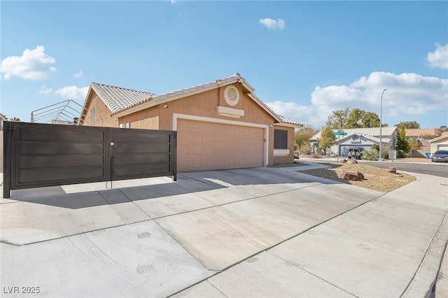 view of front facade with a gate, an attached garage, stucco siding, concrete driveway, and a tile roof