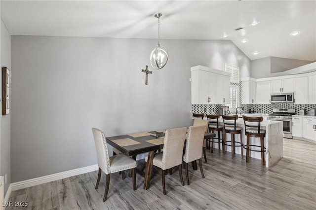 dining area with visible vents, light wood-style flooring, baseboards, a chandelier, and vaulted ceiling