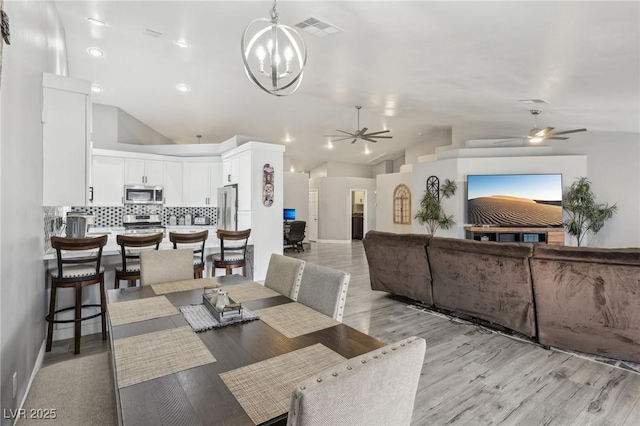 dining area featuring visible vents, light wood finished floors, baseboards, vaulted ceiling, and ceiling fan with notable chandelier