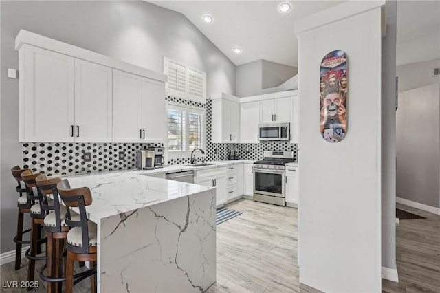 kitchen featuring a sink, light stone counters, tasteful backsplash, appliances with stainless steel finishes, and a peninsula