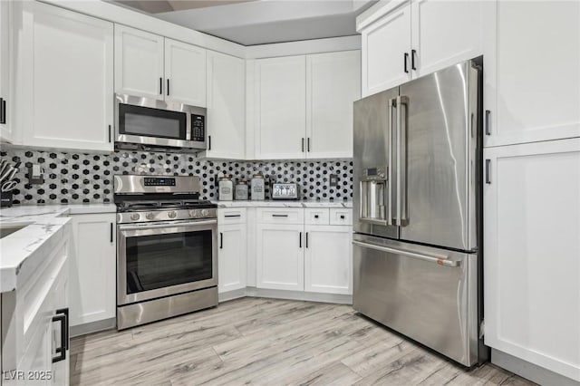 kitchen with light wood finished floors, light stone counters, decorative backsplash, stainless steel appliances, and white cabinetry