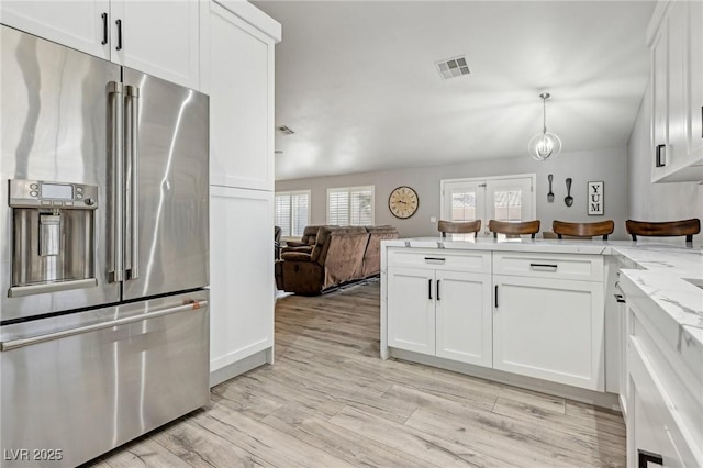 kitchen with visible vents, a peninsula, high end fridge, white cabinets, and open floor plan