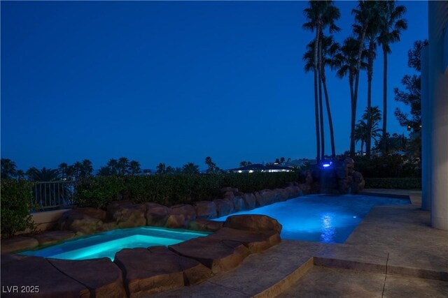 pool at night with a patio area and an outdoor pool