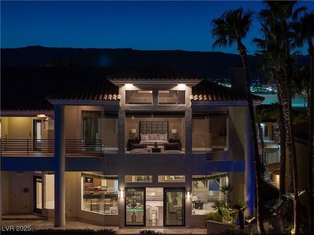 back of house at twilight with an outdoor living space, stucco siding, a balcony, and a tiled roof