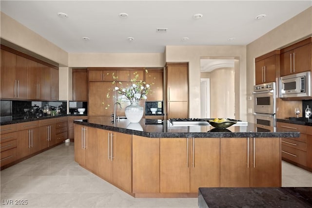 kitchen with dark stone countertops, visible vents, tasteful backsplash, and stainless steel appliances