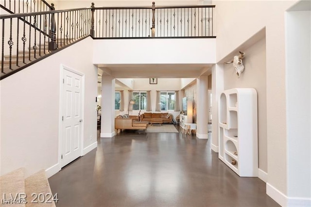 foyer entrance with baseboards, concrete flooring, and a high ceiling