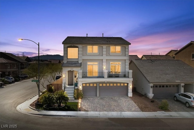 view of front of property with decorative driveway, a balcony, an attached garage, and stucco siding