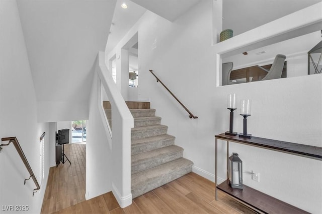 stairs with a towering ceiling, recessed lighting, baseboards, and wood finished floors