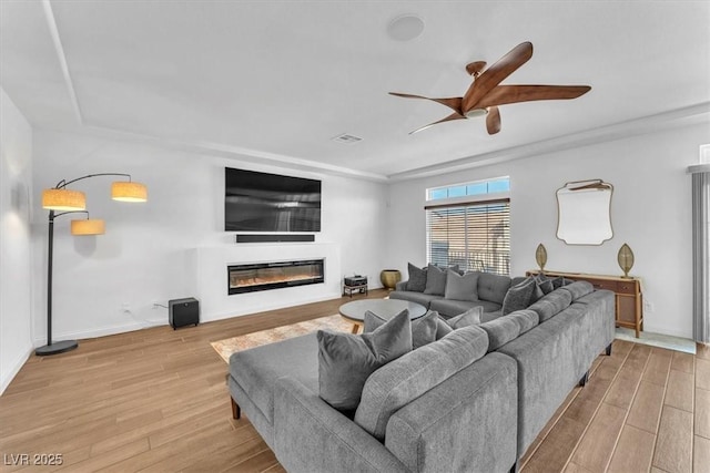 living room with visible vents, baseboards, ceiling fan, wood finished floors, and a glass covered fireplace