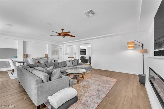 living area with a glass covered fireplace, baseboards, visible vents, and light wood finished floors