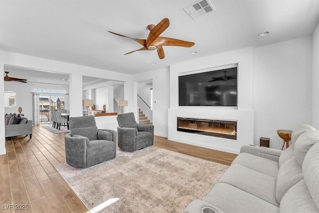 living room featuring ceiling fan, visible vents, wood finished floors, and a glass covered fireplace