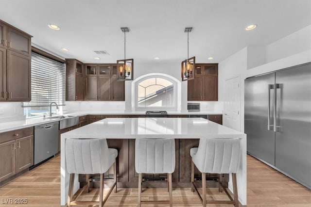 kitchen with visible vents, a breakfast bar, a sink, glass insert cabinets, and appliances with stainless steel finishes