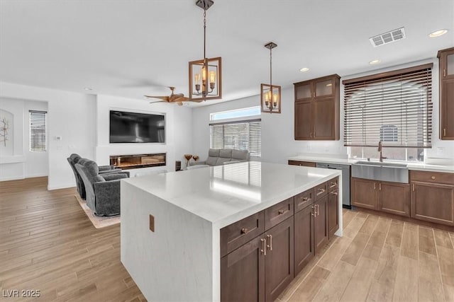 kitchen with a glass covered fireplace, dishwasher, light wood-style floors, and visible vents