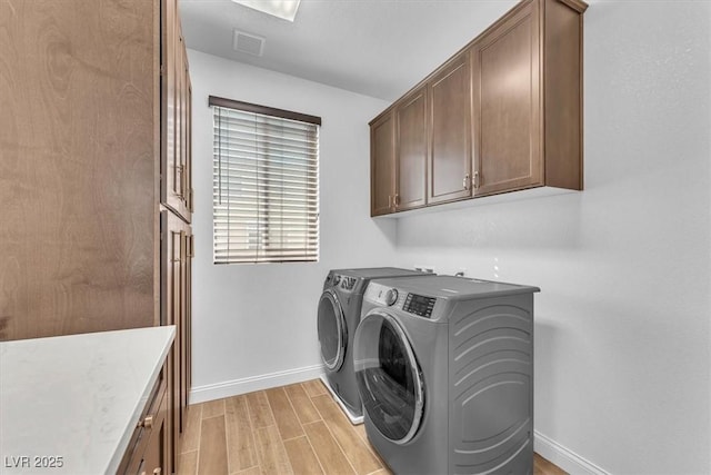 washroom with visible vents, cabinet space, baseboards, wood tiled floor, and washing machine and clothes dryer