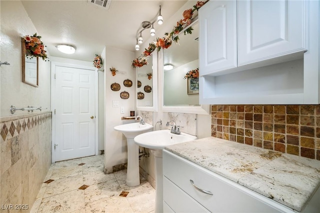 full bathroom with tile walls, visible vents, and two sinks