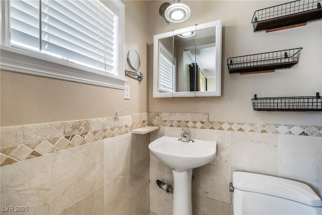 half bath with toilet, tile walls, and wainscoting