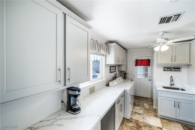 kitchen featuring light stone countertops, visible vents, a sink, stone finish floor, and washing machine and dryer