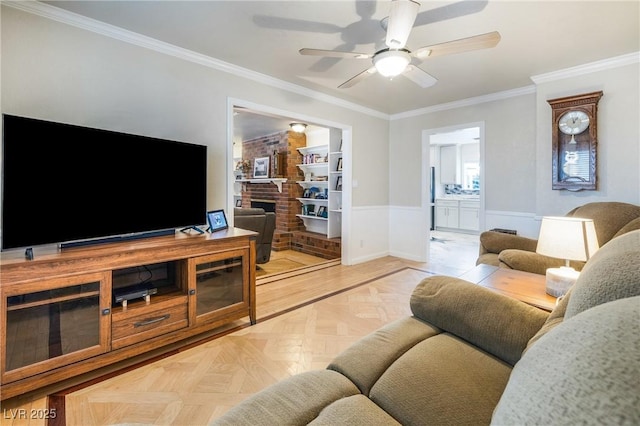 living room featuring a wainscoted wall, a brick fireplace, ceiling fan, and ornamental molding