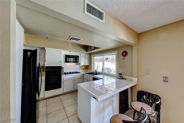 kitchen with visible vents, light tile patterned floors, a peninsula, black appliances, and a sink